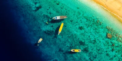 Aerial view of boats in turquoise coastal water beside a sandy beach
