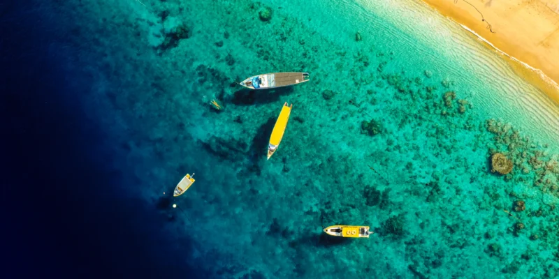 Aerial view of boats in turquoise coastal water beside a sandy beach