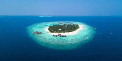 Aerial view of a tree-covered island with a white beach and turquoise lagoon in the Maldives