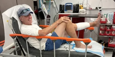 John Schweizer sits on a hospital bed after the shark bite in the Bahamas with his left lower leg bandaged