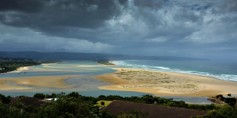 View across the lagoon, beach and ocean at Plettenberg Bay under dark storm clouds